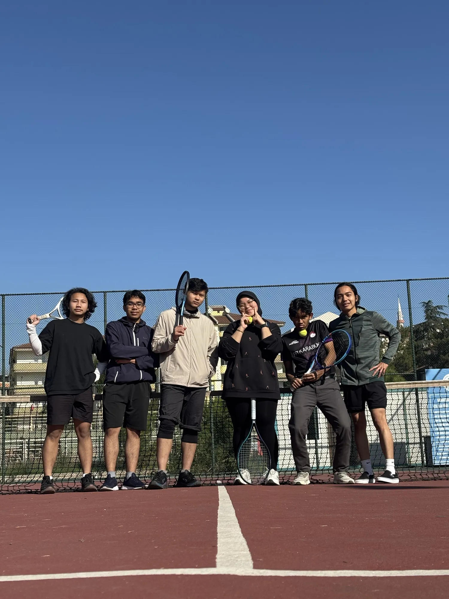 Seven friends holding rackets, lined up on a tennis court