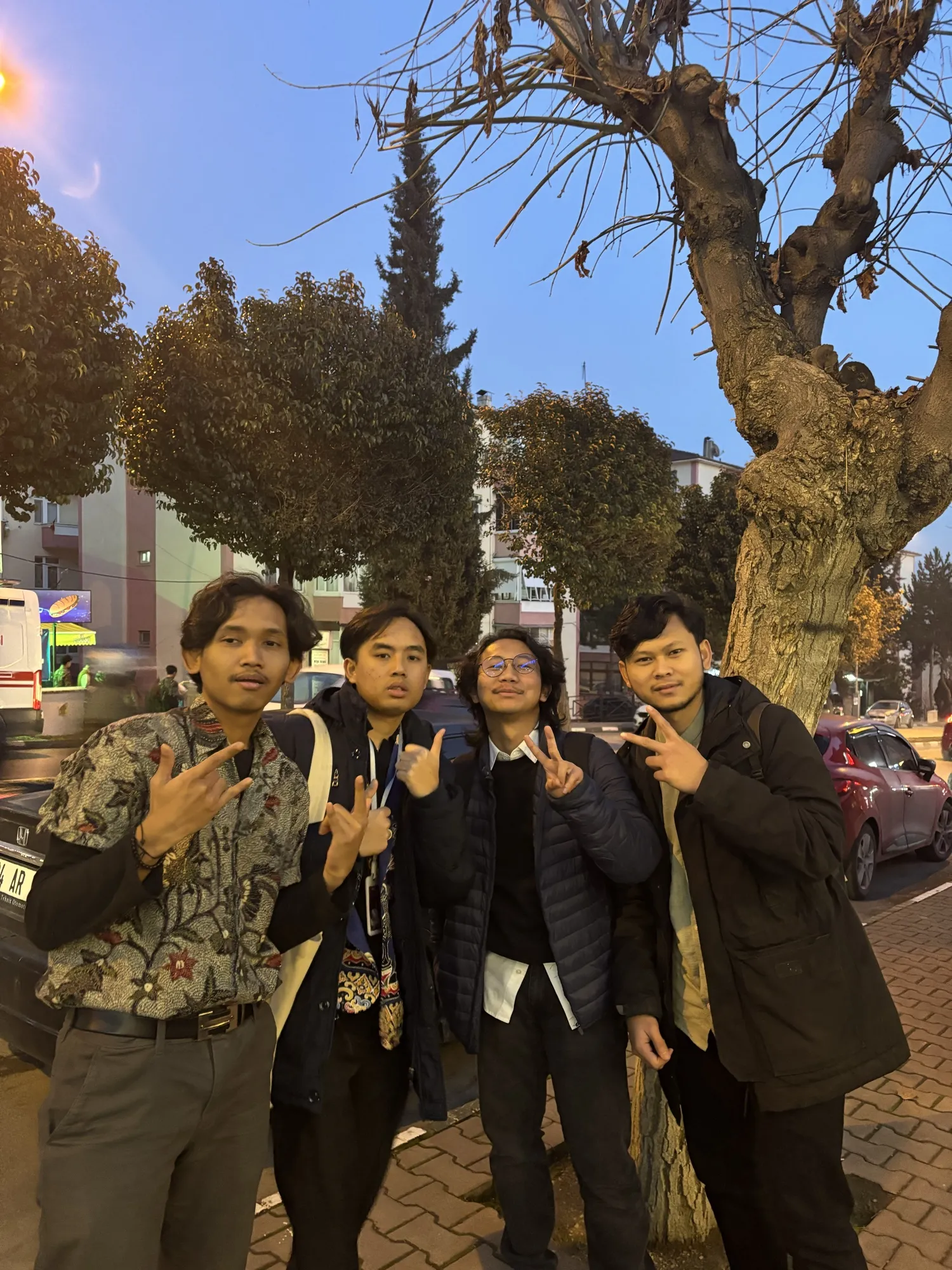 Four friends making hand signs on a street at dusk