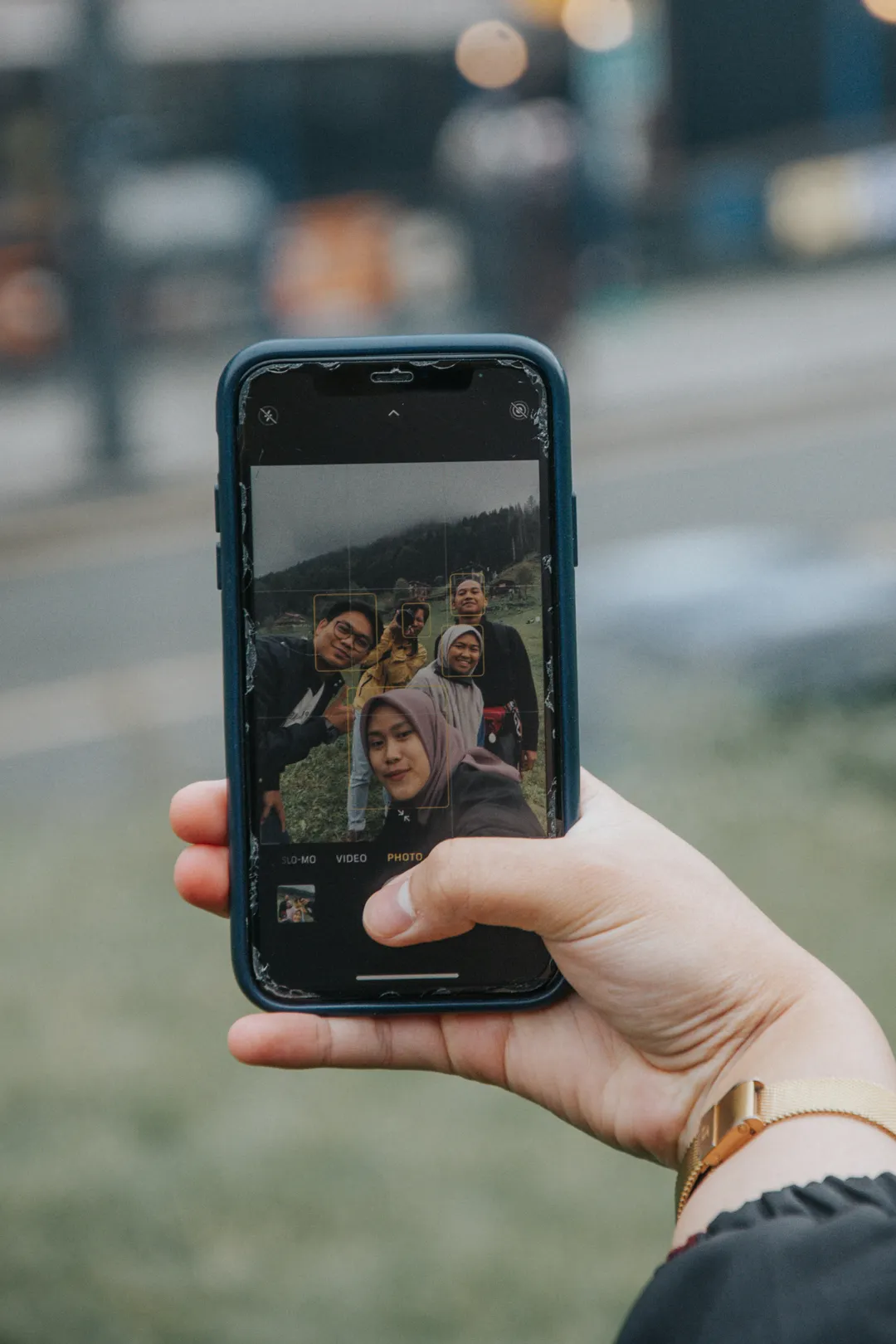 A hand holding up a phone that shows a group selfie on a grassy hill