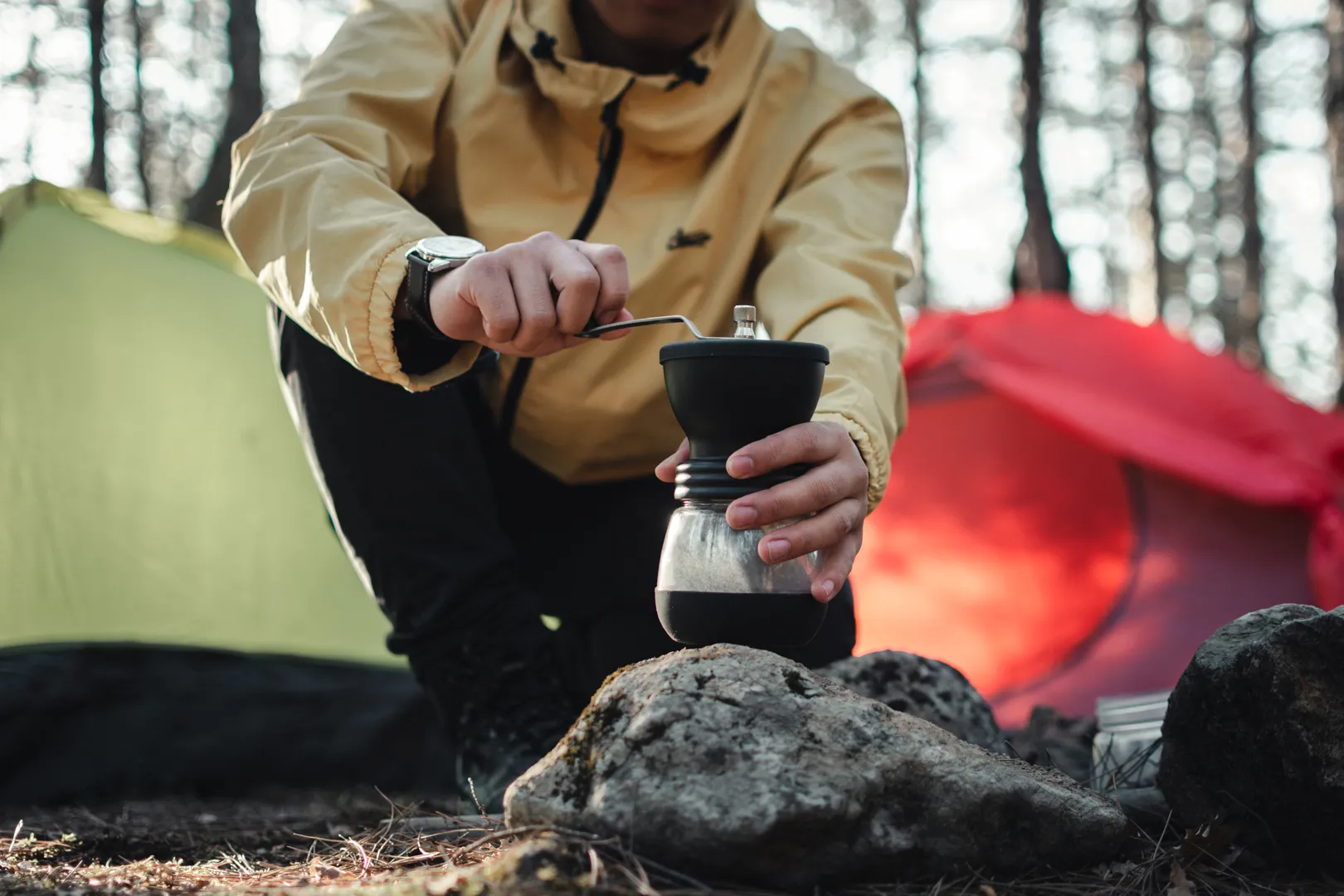 Grinding coffee by hand on a rock between two tents