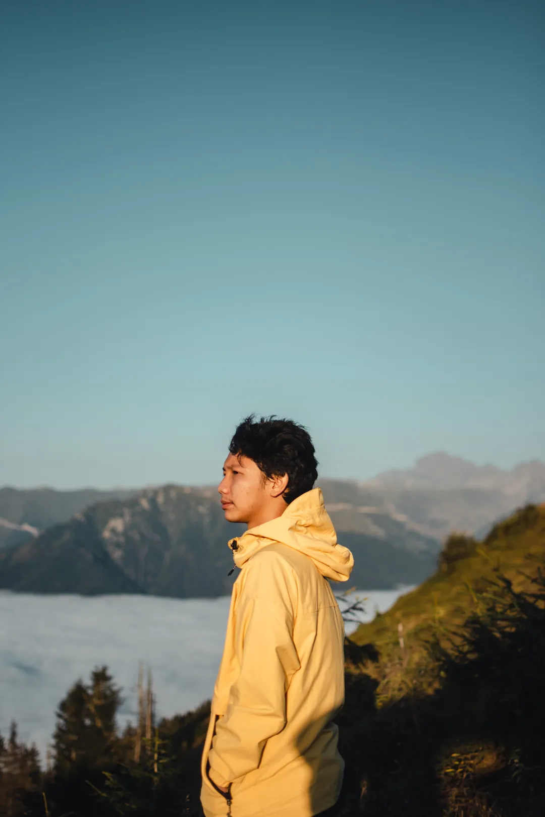 Hasbii in a yellow hoodie on a mountain ridge above a sea of clouds