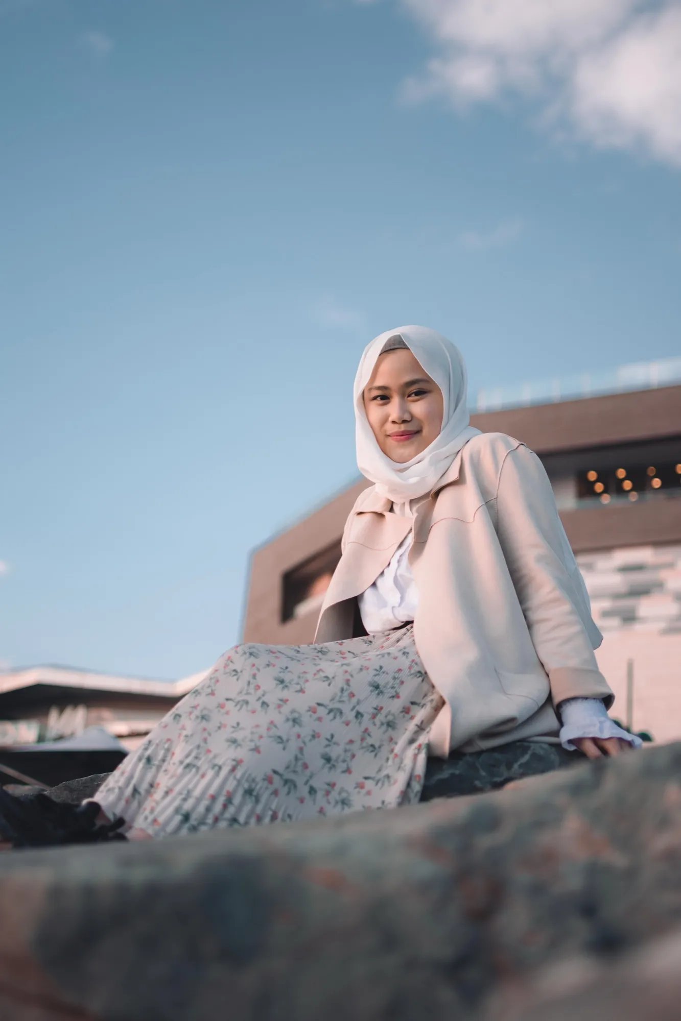 A woman in a white hijab sitting on a rock under a blue sky
